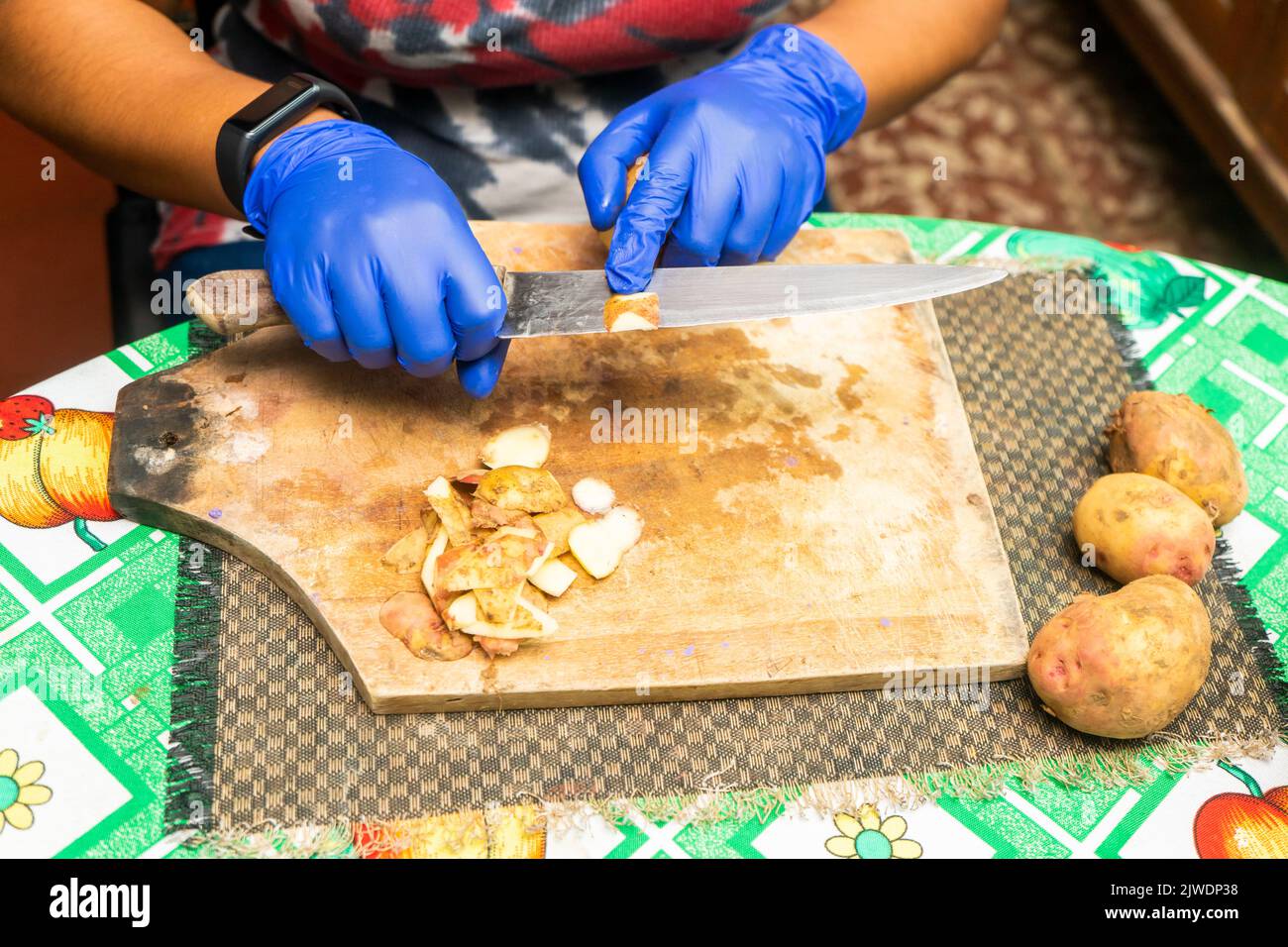 Eine nicht erkennbare Lateinerin schälte Kartoffeln mit blauen Handschuhen in ihrer Küche zu Hause Stockfoto