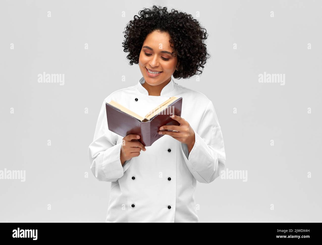 Lächelnde Köchin beim Lesen des Kochbuches Stockfoto