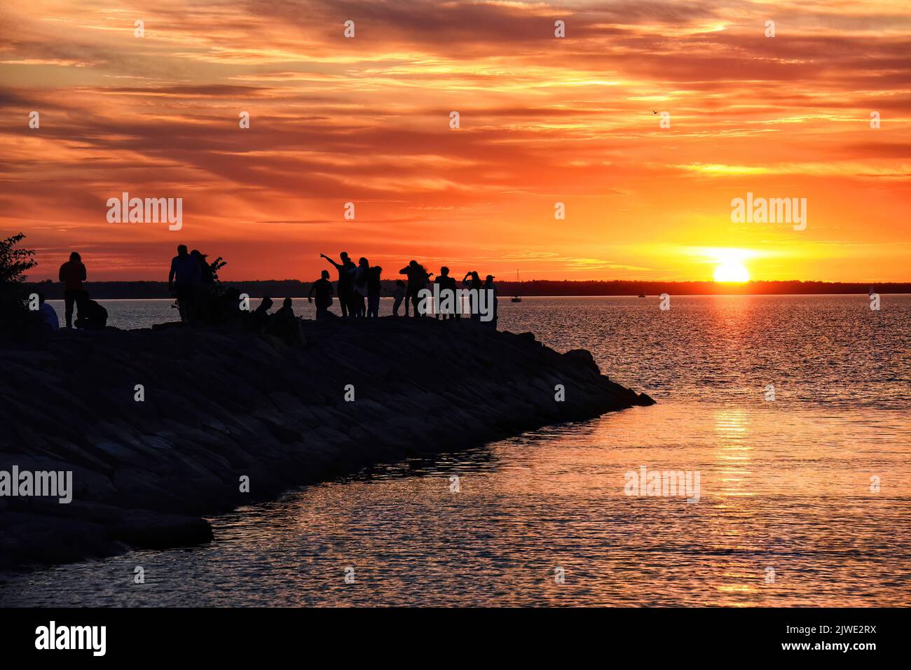 Auf dem Wellenbrecher versammeln sich Menschen, um den Sonnenuntergang auf dem Ottawa River zu beobachten Stockfoto