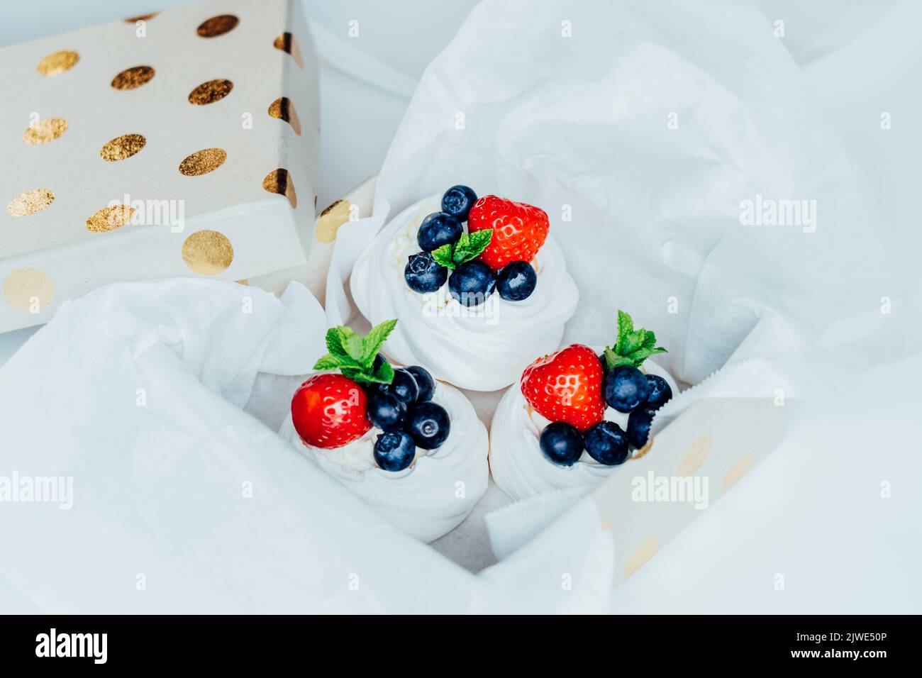 Set aus Pavlova-Baiser-Dessertkuchen mit frischen Erdbeeren und Blaubeeren, dekoriert mit Minze in Geschenkbox verpackt. Süße Präsens Idee. Festliche Foo Stockfoto