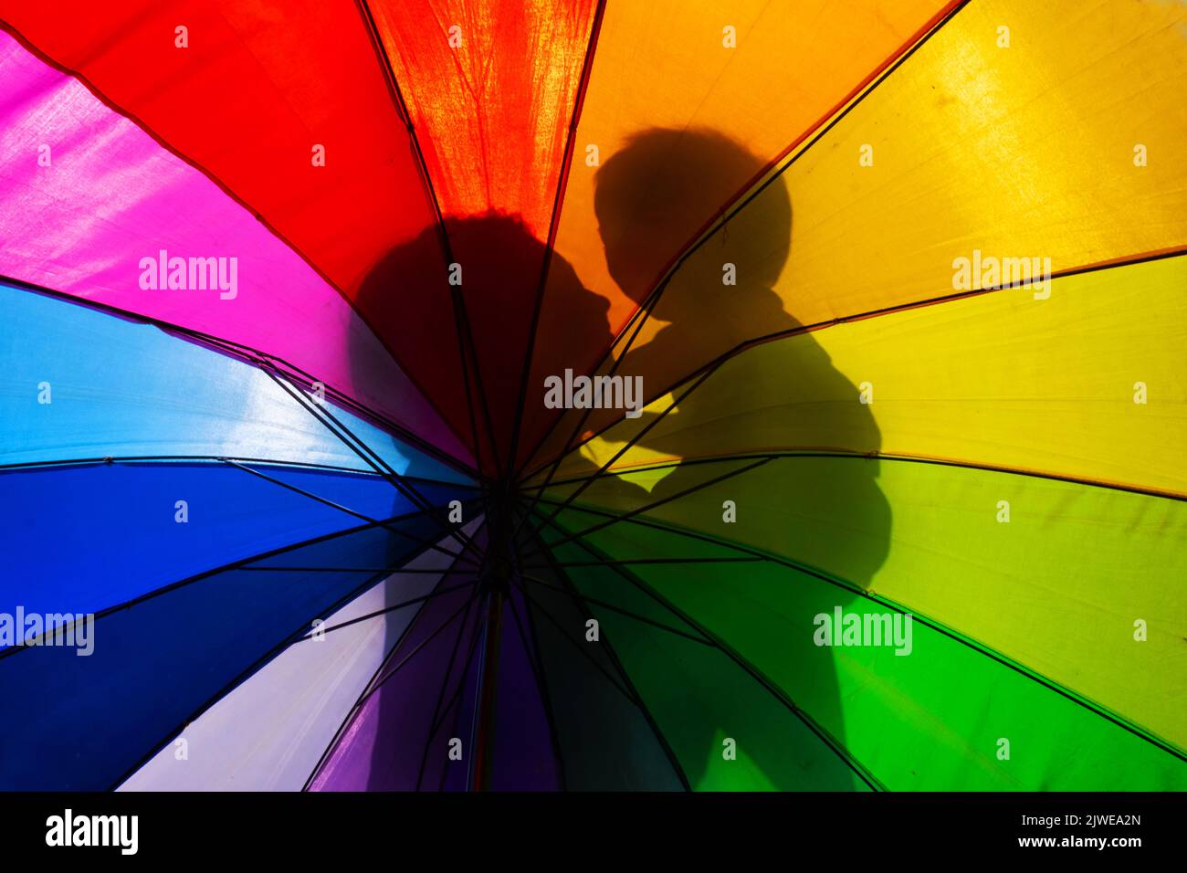 Silhouette einer Mutter, die ein Kind durch einen bunten Regenschirm hält Stockfoto