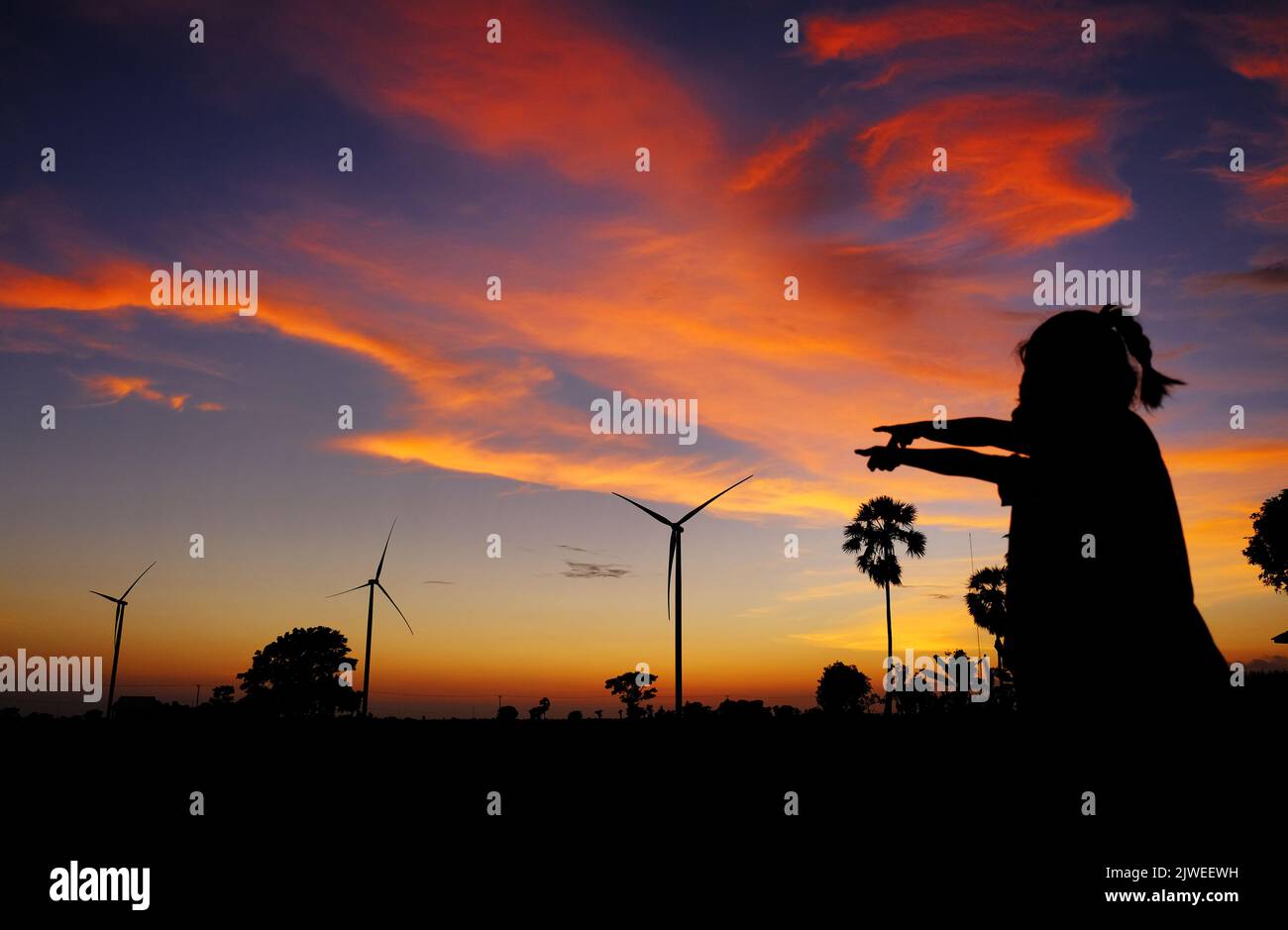 Silhouette von zwei Mädchen, die bei Sonnenuntergang auf Windturbinen zeigen, Jeneponto, Süd-Sulawesi, Indonesien Stockfoto