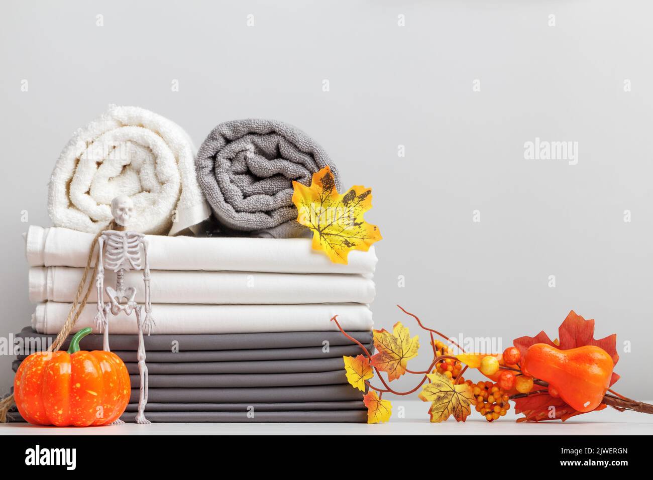 Ein Stapel Bettwäsche, ein Bettlaken und gefaltete Handtuchrollen auf einem Tisch mit Halloween-Dekor. Stockfoto