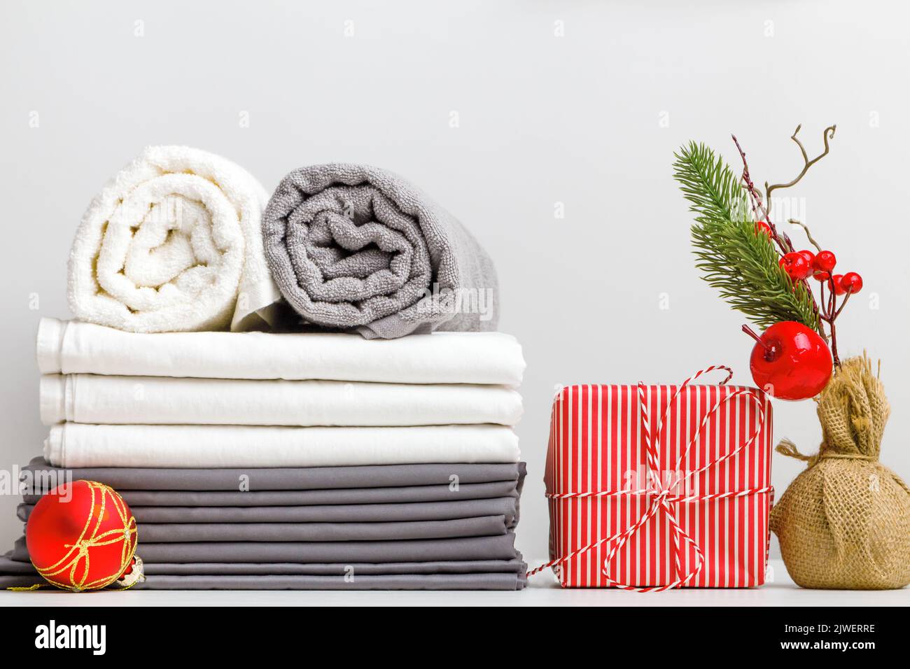 Stapel Bettwäsche, Bettwäsche und gefaltete Handtuchrollen auf einem Tisch mit weihnachtlicher Dekoration Stockfoto