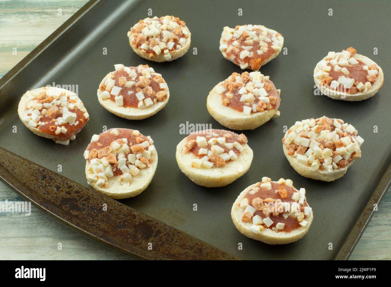 Gefrorene Mini-Pizza-Snack-Stücke in mundgroßer Größe mit Tomatensauce und Käsewürfeln auf Backblech Stockfoto