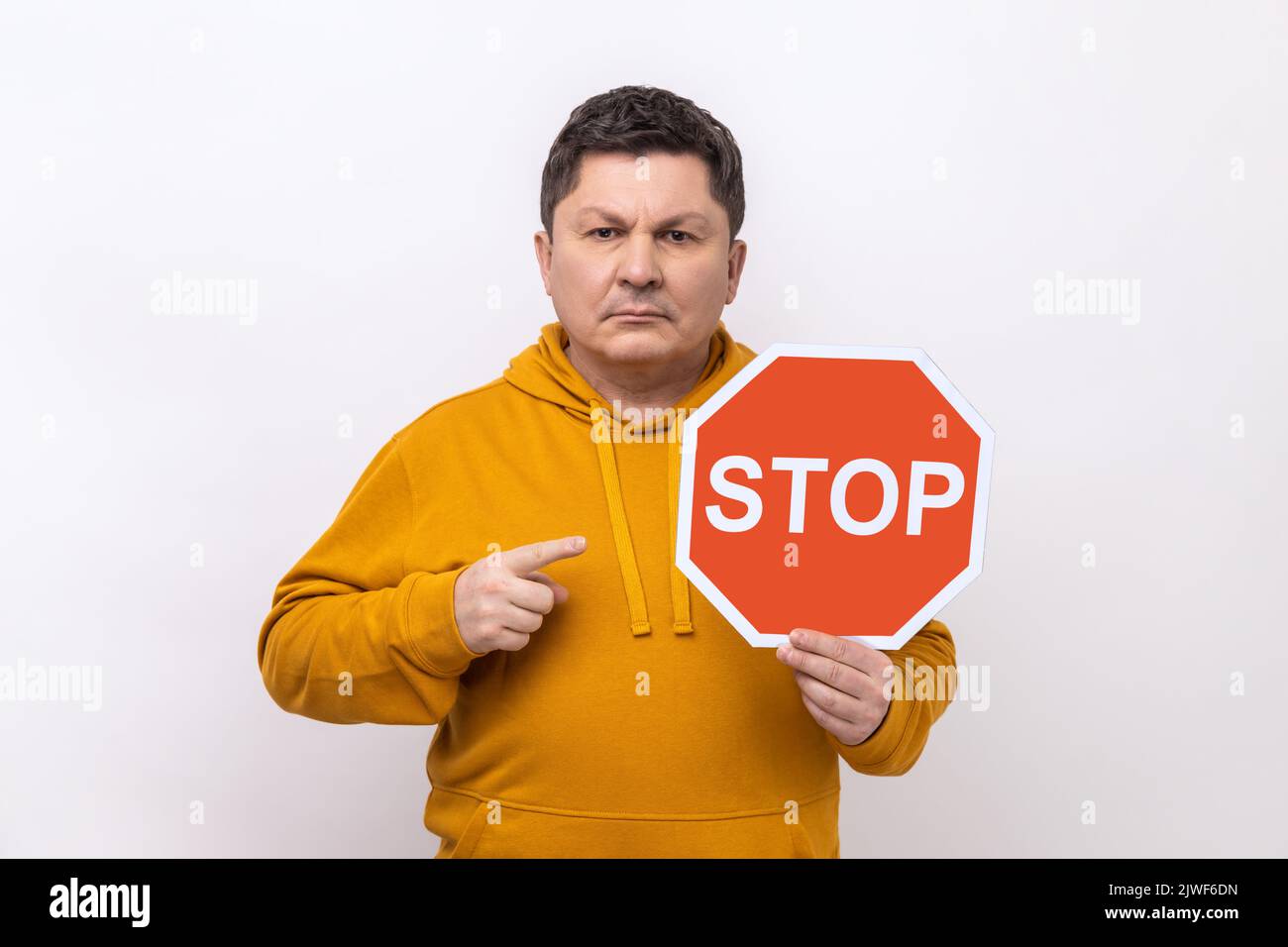 Porträt eines streng herrischen Mannes mittleren Alters, der als Symbol der Prohibition auf das Verkehrsschild Stop zeigt und einen Hoodie im urbanen Stil trägt. Innenaufnahme des Studios isoliert auf weißem Hintergrund. Stockfoto
