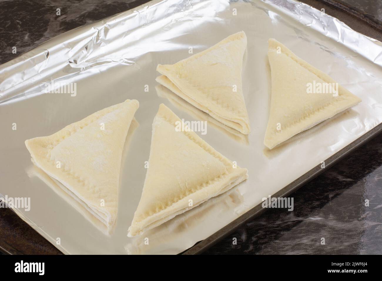 Gefrorene Apfelumschlag-Dreiecke auf verwittertem Backblech, ausgekleidet mit Aluminiumfolie Stockfoto