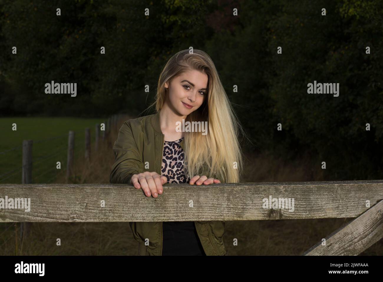 Ein hübscher blonder Teenager, der sich an ein Tor lehnt Stockfoto