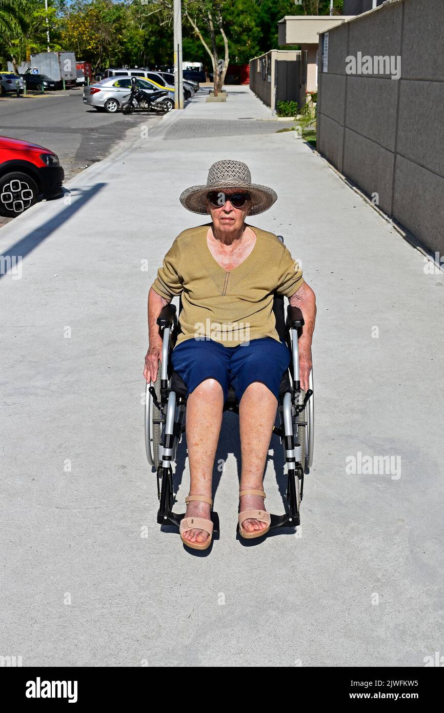 Ältere Frau, die auf dem Bürgersteig im Rollstuhl sitzt, Rio Stockfoto