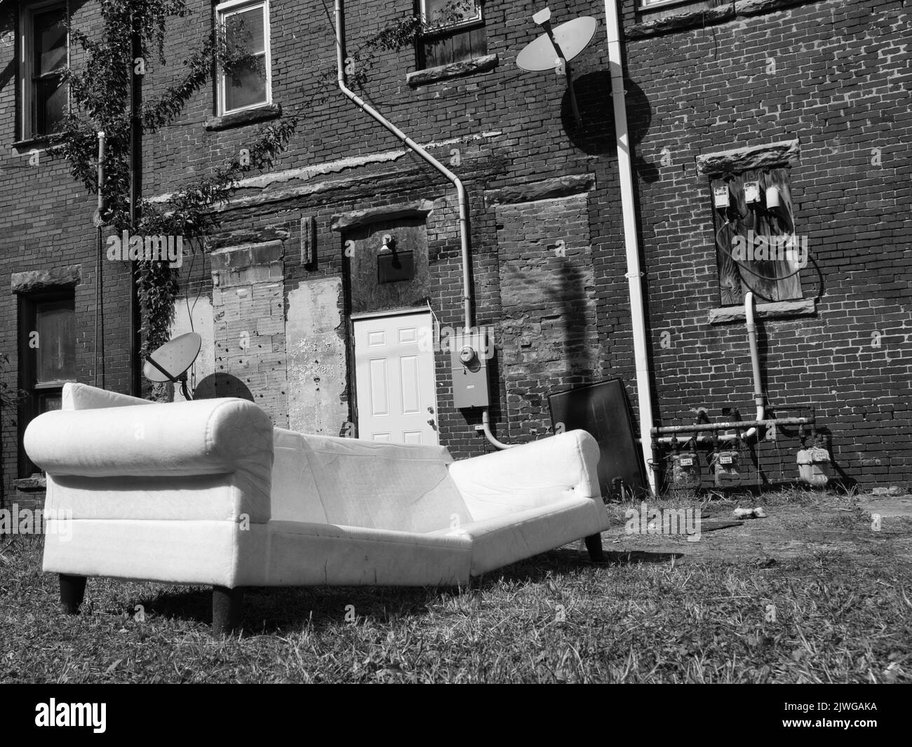 Schwarzweiß-Bild einer verlassenen Couch hinter einem Backsteingebäude Stockfoto