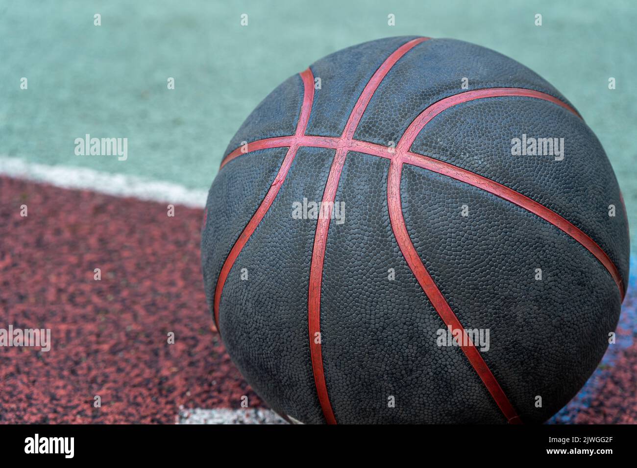 Schwarzer Basketballball auf dem Boden. Nahaufnahme des Balls auf dem Roten Platz. Basketball auf der Straße oder im Innenhof. Sportausrüstung ohne Menschen. Minimalismus. Stockfoto