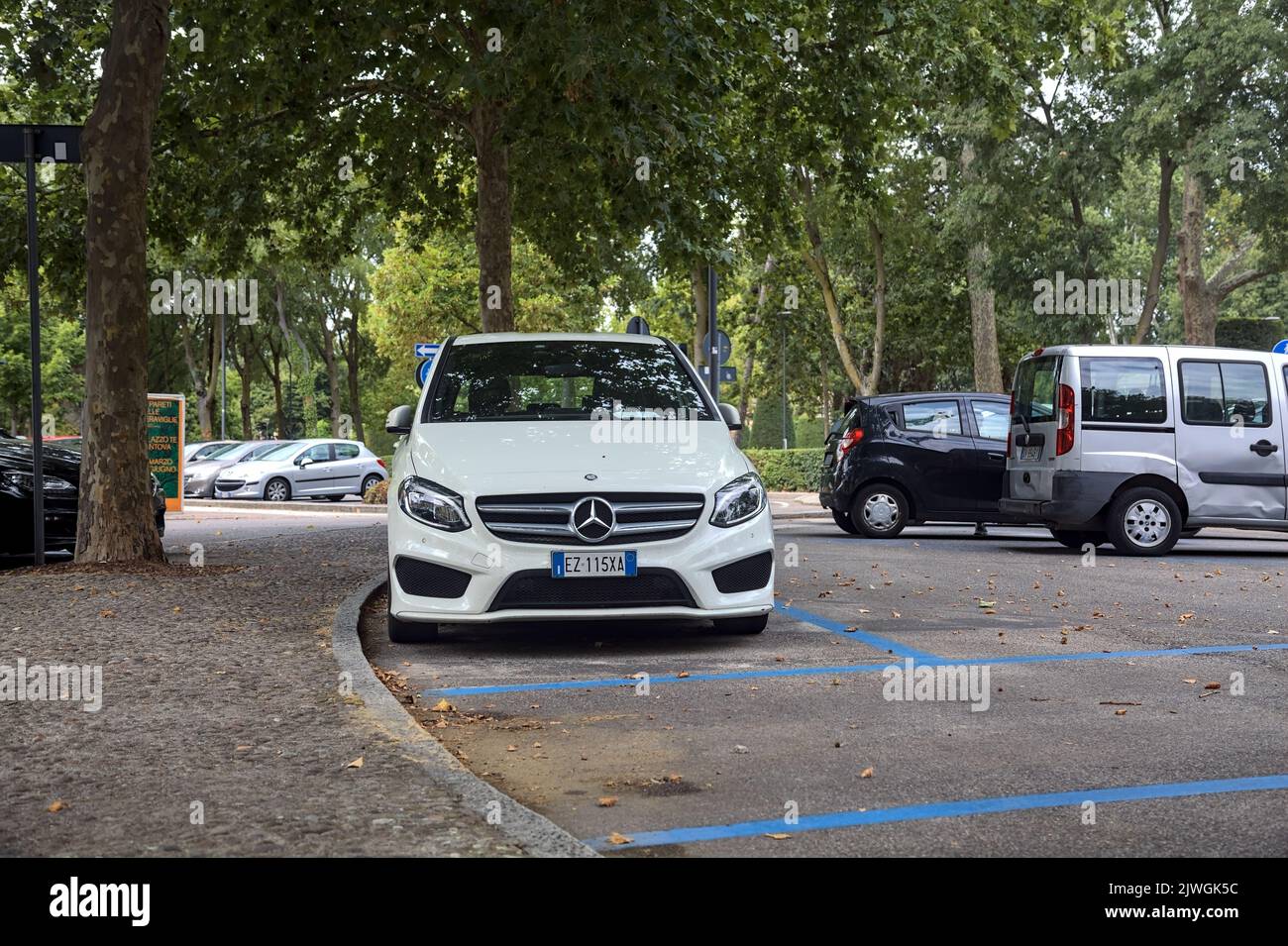Weißer Mercedes Benz C180 auf einem öffentlichen Parkplatz neben einem Park an einem bewölkten Tag Stockfoto