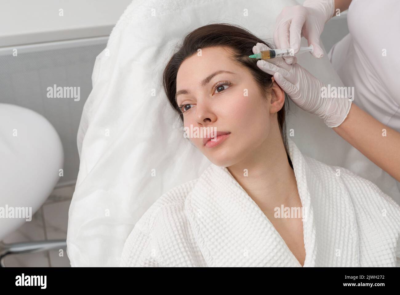 Der Arzt macht eine Injektion in den Kopf eines Mädchens aus Haarausfall. Haarbehandlung in einer Kosmetikklinik. Stockfoto