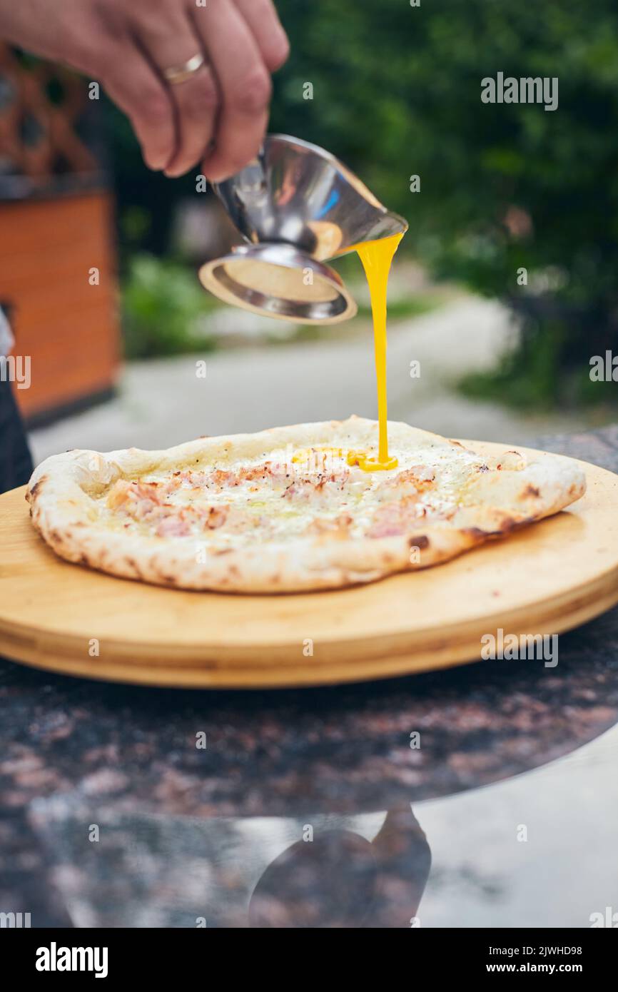 Fertig heiße Pizza wird Sauce gegossen. Der Prozess der Herstellung von hausgemachter Pizza. Das Konzept der hausgemachten Fast Food. Vertikales Foto. Stockfoto