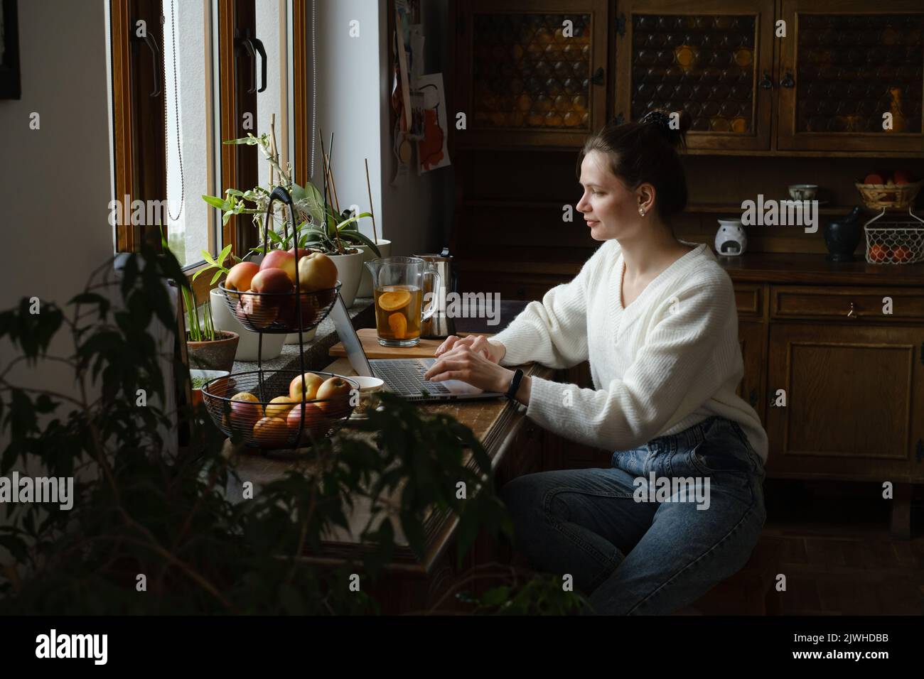 Junge Freiberuflerin, die zu Hause am Laptop arbeitet. Frau, die Computer in der Küche zur Arbeit benutzt. Entfernter Job, Remote-Arbeit in gemütlichen Vintage-Haus Stockfoto