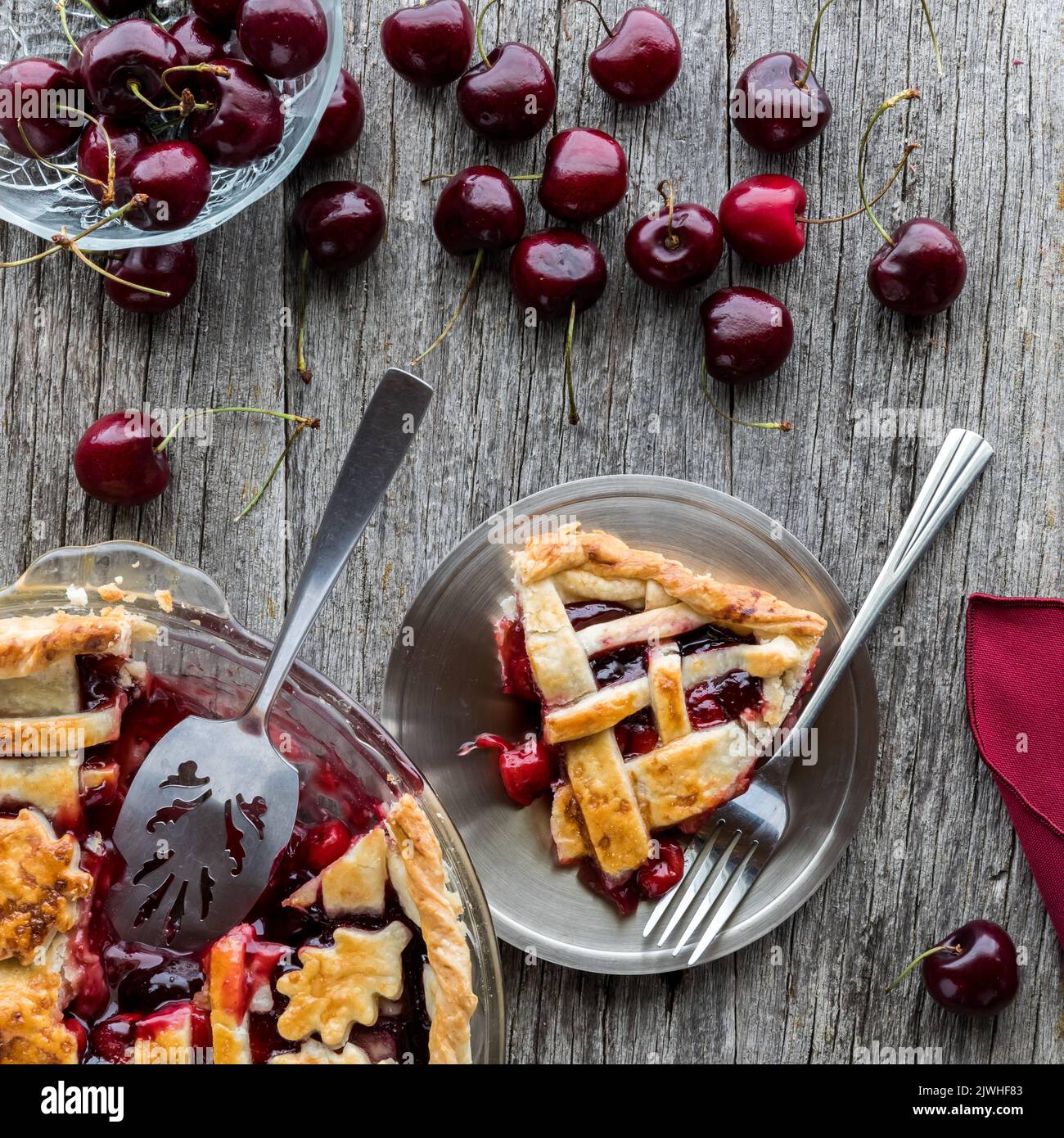 Eine Portion Kirschkuchen mit dem vollen Kuchen links und Kirschen oben. Stockfoto