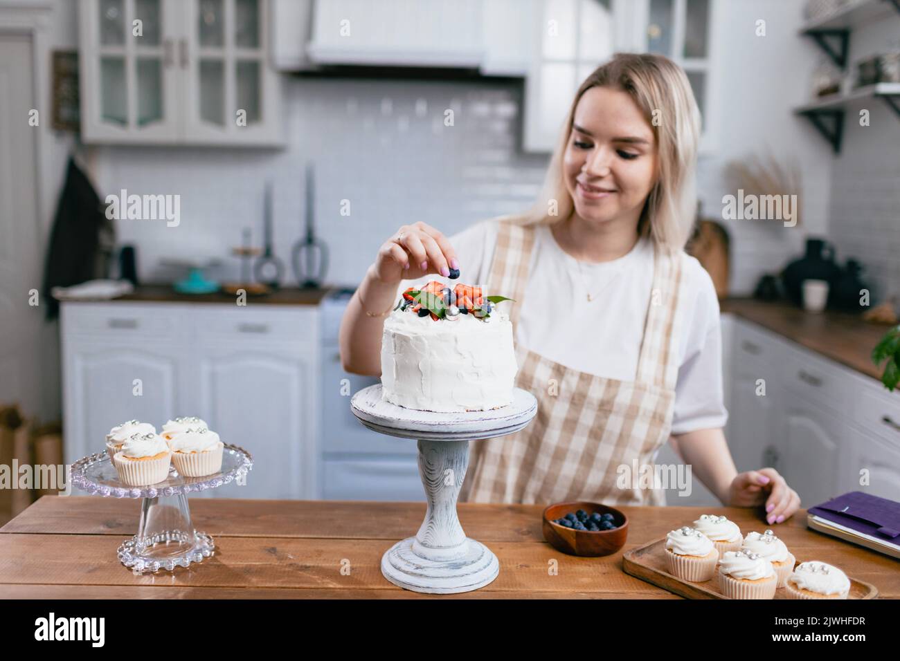 Konditor Konditor junge kaukasische Frau dekorieren Kuchen auf Küchentisch. Kuchen Cupcakes und süßes Dessert Stockfoto
