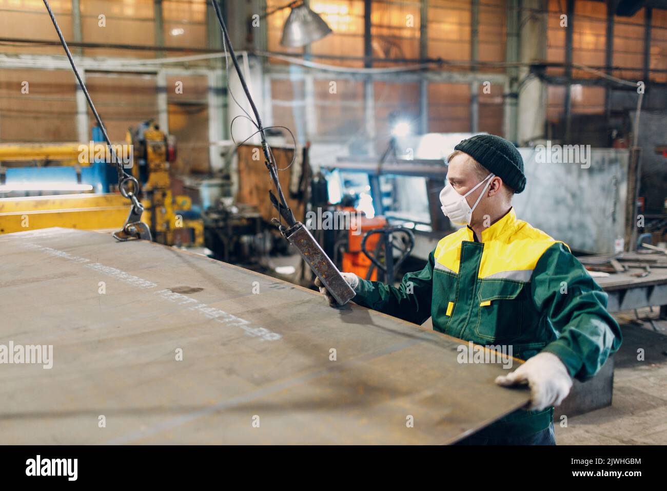 Arbeiter heben Metallblech mit Krankettenzug mit Fernbedienung und Haken in der industriellen Fabrik Stockfoto