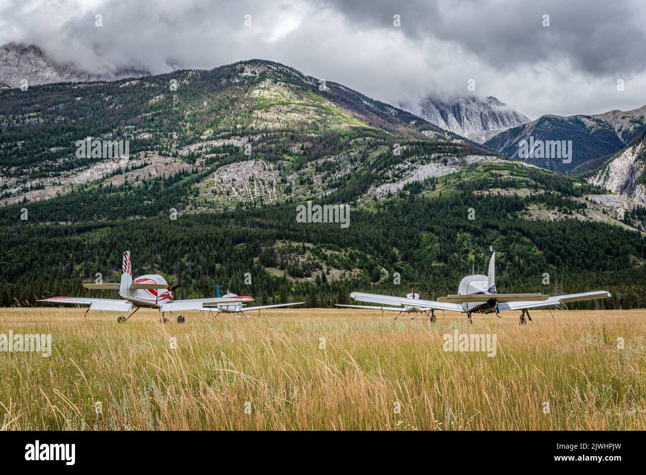 Vier Flugzeuge, die auf dem Jasper Airstrip in der Nähe von Jasper, Alberta, mit Bergen im Hintergrund festgebunden sind Stockfoto