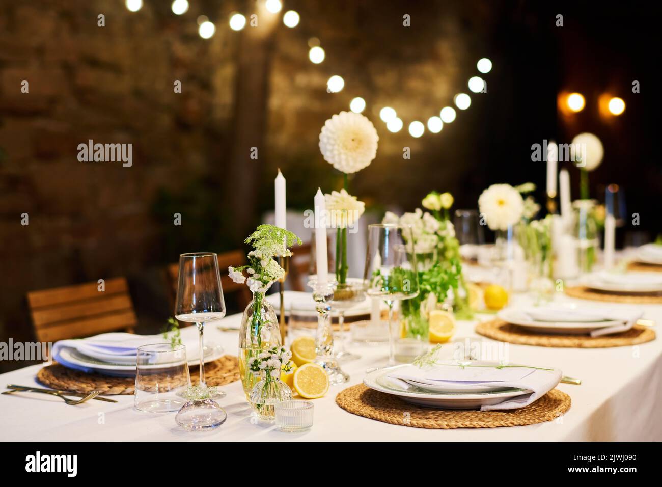 Festlicher Tisch mit zwei Reihen von Tellern mit Servietten, die Kerzen umgeben, Blumen in Vasen und Weingläser, die für das Hochzeitsfest vorbereitet sind Stockfoto