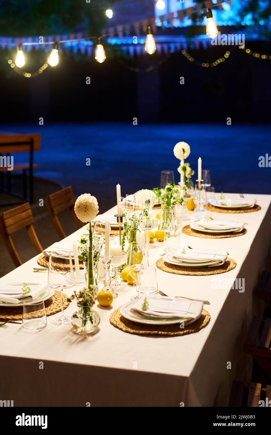 Langer Tisch mit weißer Tischdecke mit Dahlia-Blumen, Kerzen, Dekorationen und Weingläser, umgeben von zwei Tellerreihen Stockfoto