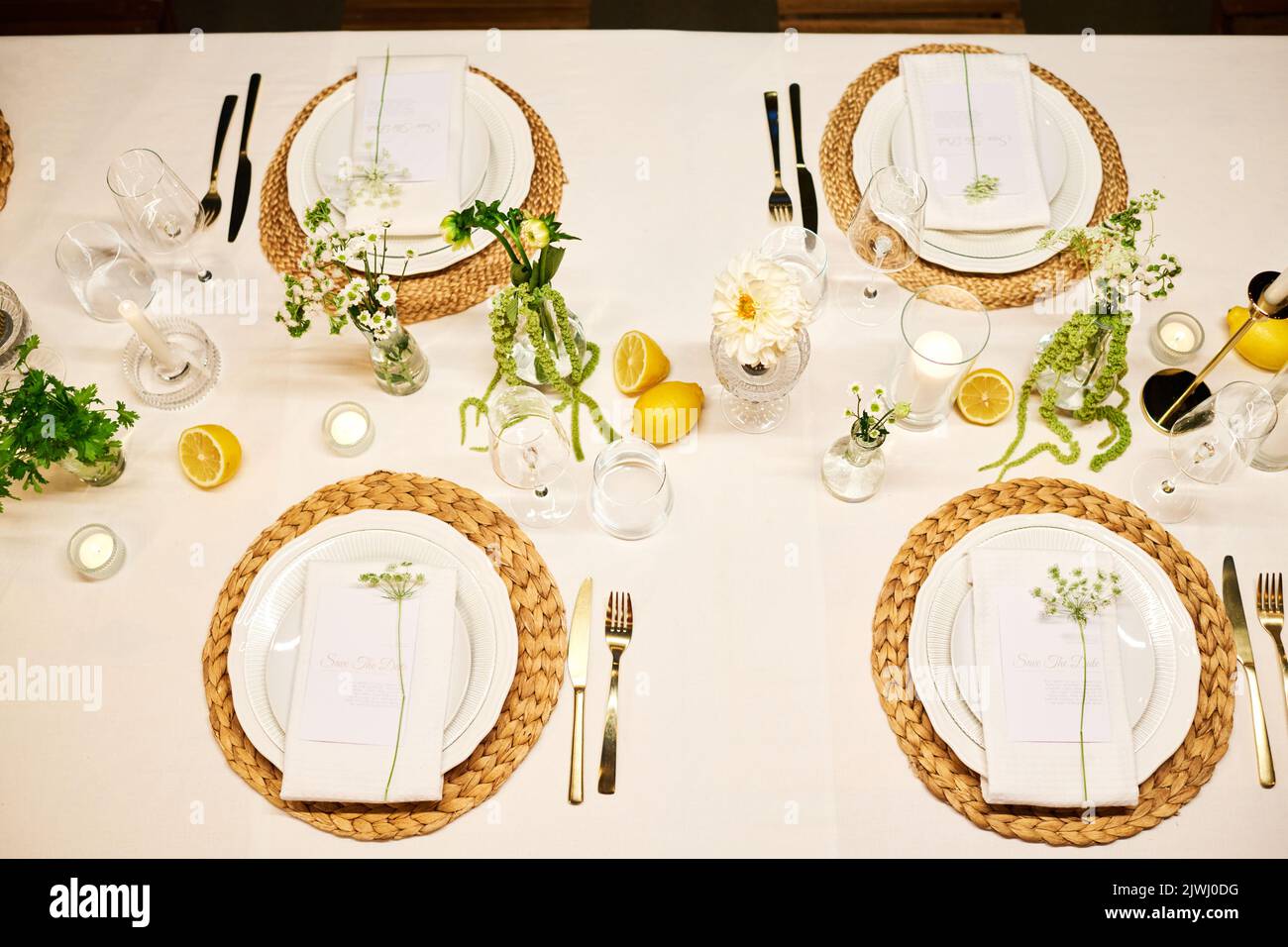 Draufsicht auf einen Teil des servierten Esstisches mit Tellern, Servietten, Weinläsern, Zitronen, Blumen und Kerzen, die für die Hochzeitsfeier vorbereitet wurden Stockfoto