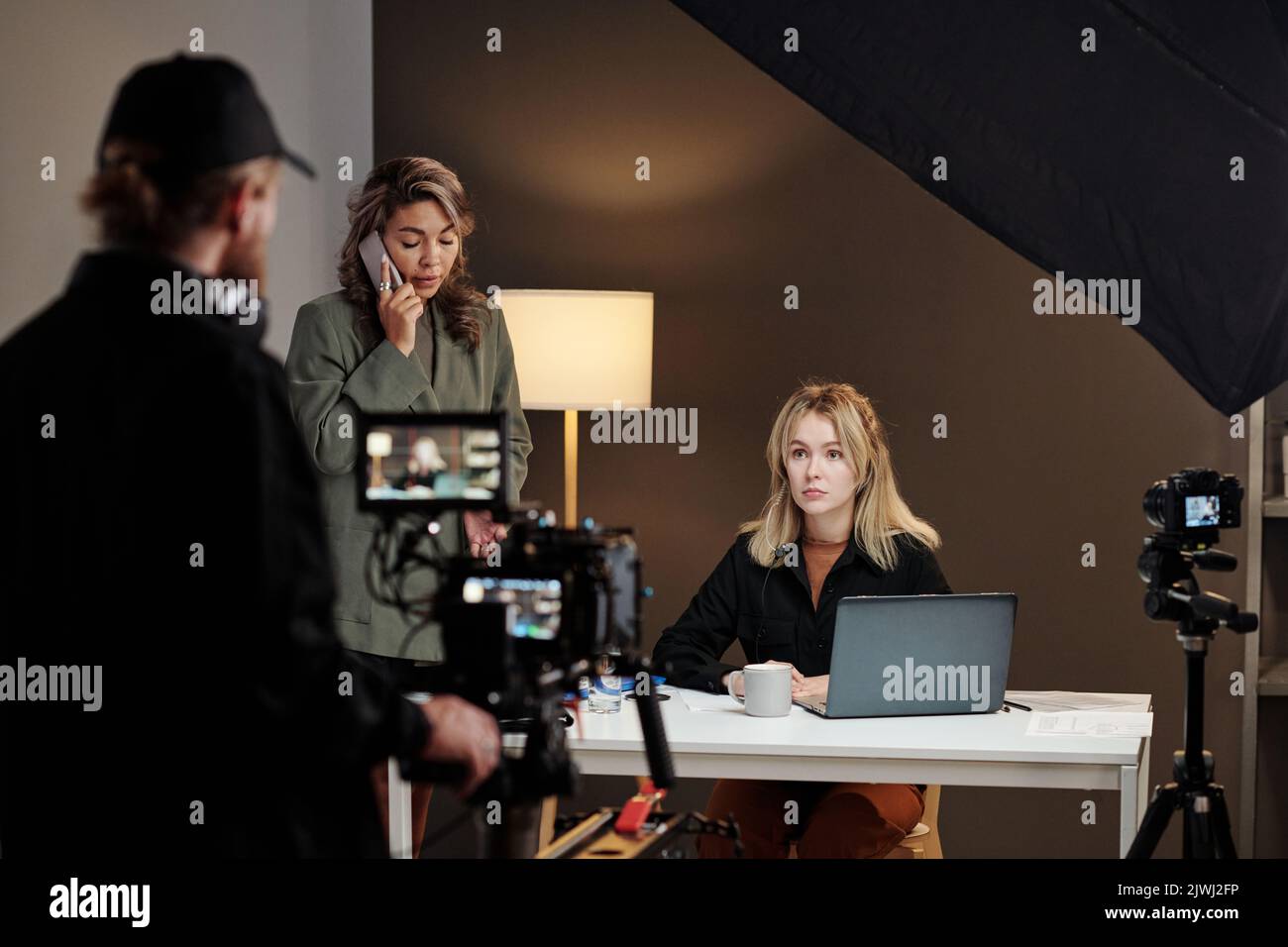 Zwei junge interkulturelle weibliche Models, die mobile Gadgets während des Werbefilms von Videofilmerin mit steadicam verwendeten Stockfoto