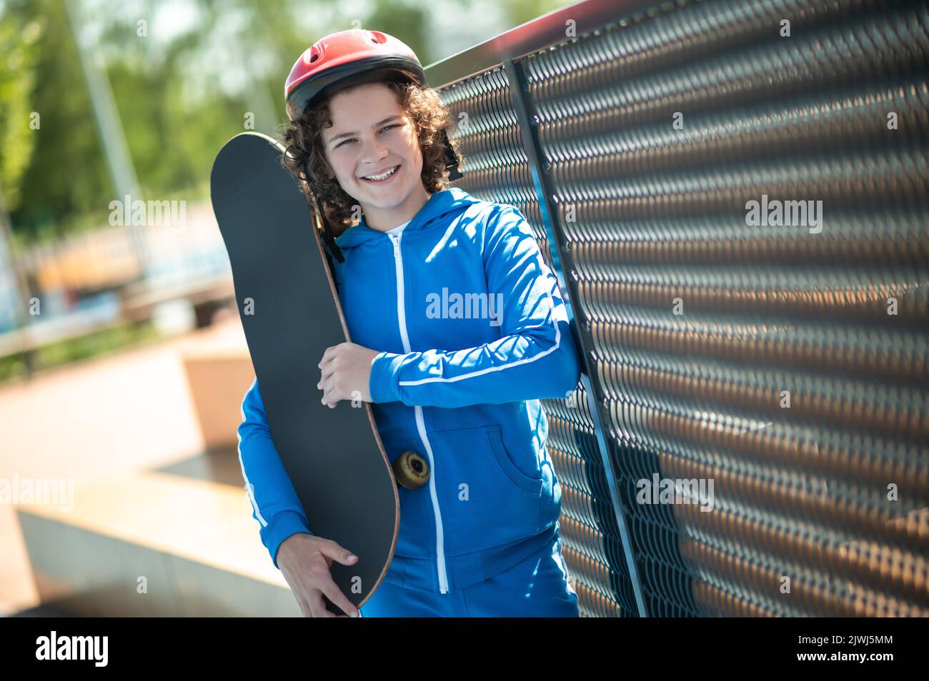 Fröhlicher Skateboarder posiert für die Kamera gegen den Kettengliedzaun Stockfoto