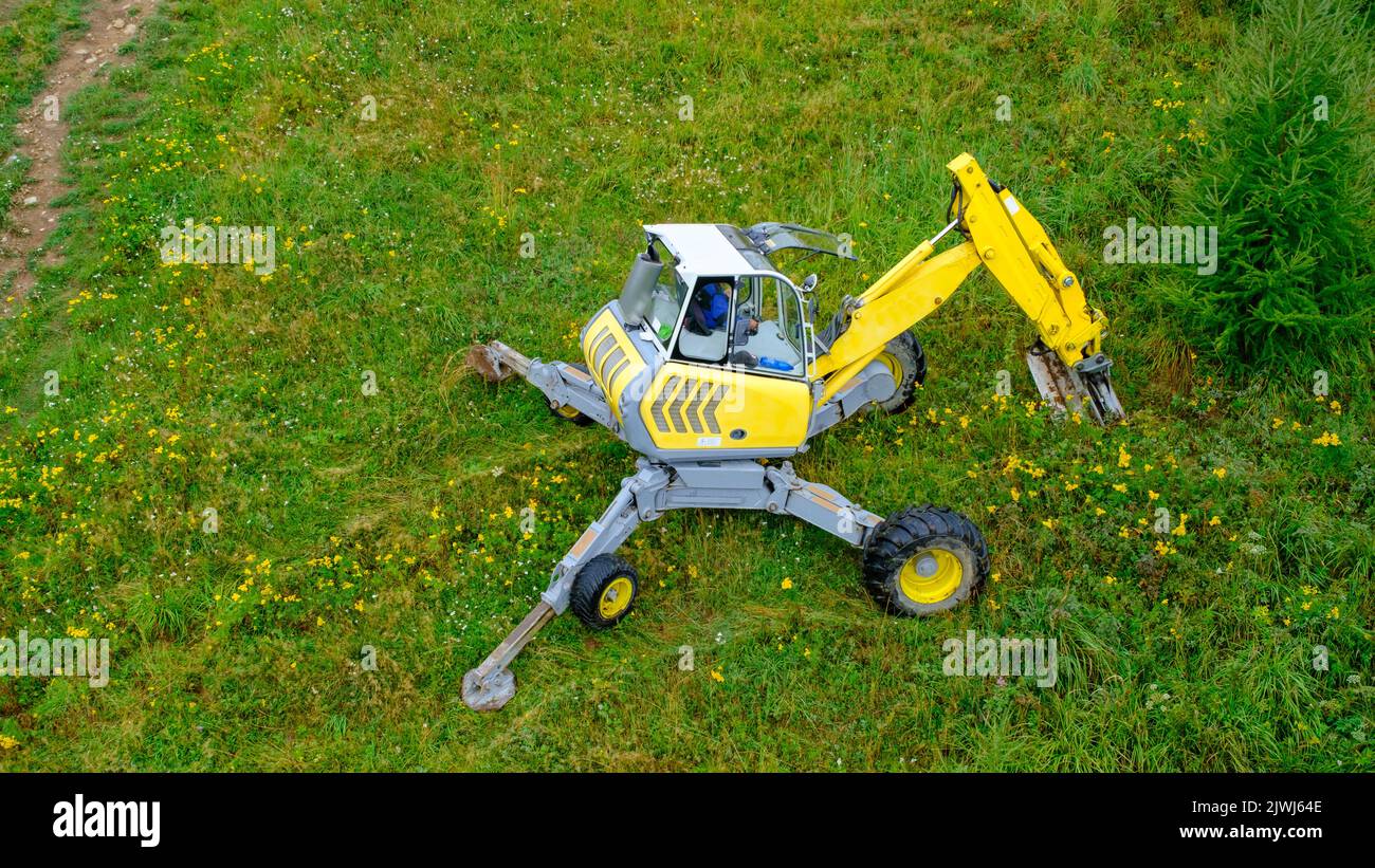 Ein kleiner gelber Bagger gräbt einen Regenwasserablauf am Fuße eines Hügels. Stockfoto