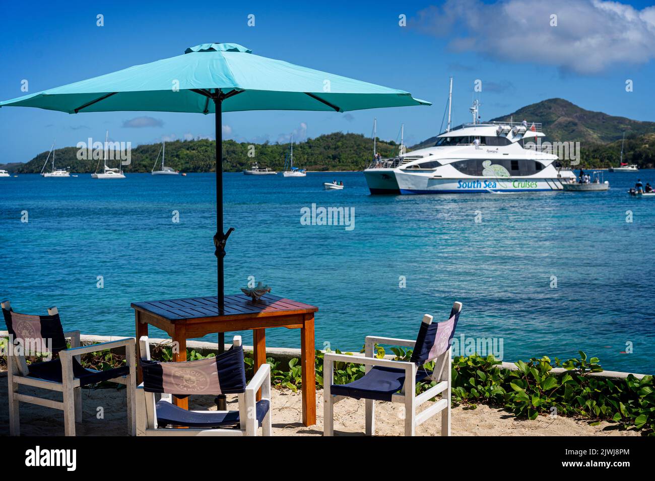 Die Yasawa Flyer-Fähre bringt Passagiere im Nanuya Island Resort mit Sonnenschirm und Tisch und Stühlen im Vordergrund ab. Fidschi Stockfoto