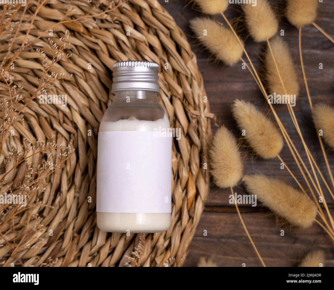 Kosmetikflasche auf Boho watschelte Tischset in der Nähe von Hare's Tail Grass Draufsicht auf Holz, Label-Mockup. Natürliches Hautpflegeprodukt, Creme oder Lotion. Böhmische ec Stockfoto