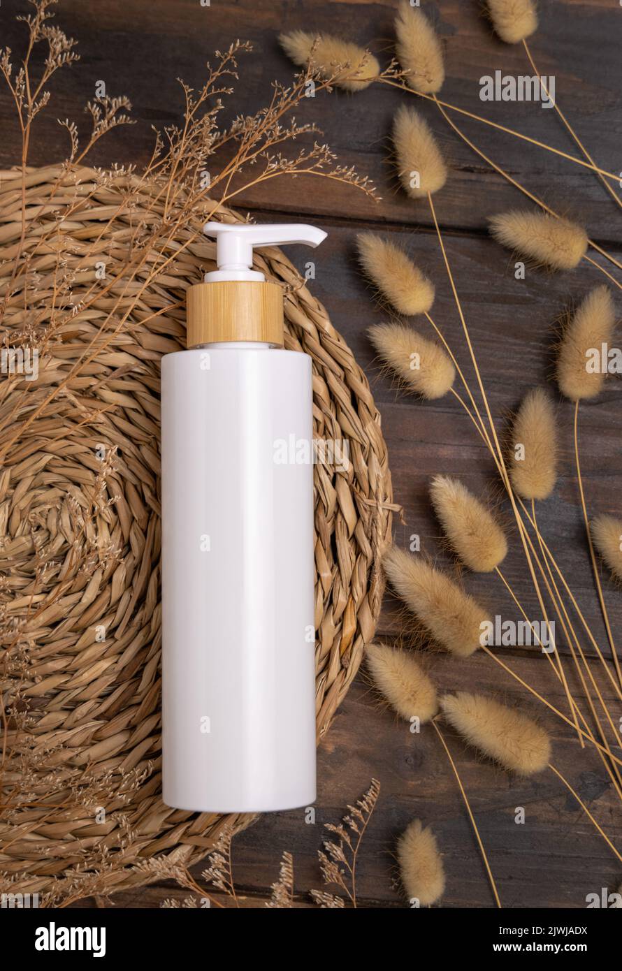 Kosmetische Flasche mit einer Pumpe auf einem Boho-Wattplacemat in der Nähe von Hare's Tail Grass, Draufsicht auf Holz, Etikettenmockup. Natürliches Hautpflegeprodukt, Creme oder Lotion. Bo Stockfoto