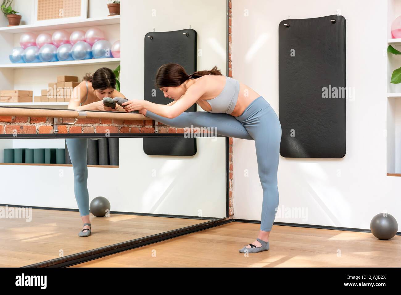 Frau, die in einem Barre in einer Turnhalle Beinstreckübungen in einem Gesundheits- und Fitnesskonzept macht, das sich in einem Wandspiegel widerspiegelt Stockfoto