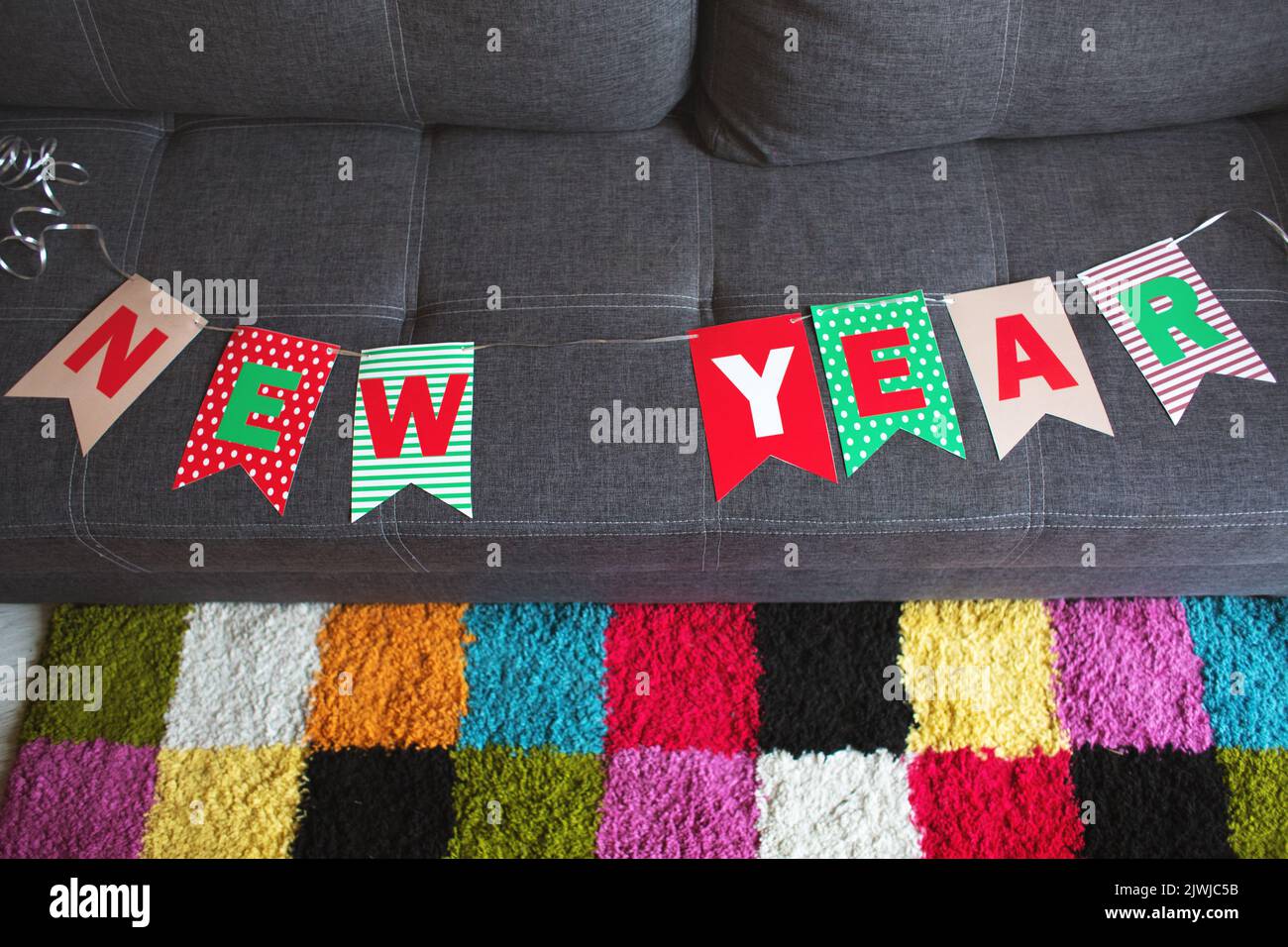 Eine Girlande aus Fahnen mit der Aufschrift Happy New Year, auf einem grauen Sofa vor dem Hintergrund eines farbigen Teppichs Stockfoto