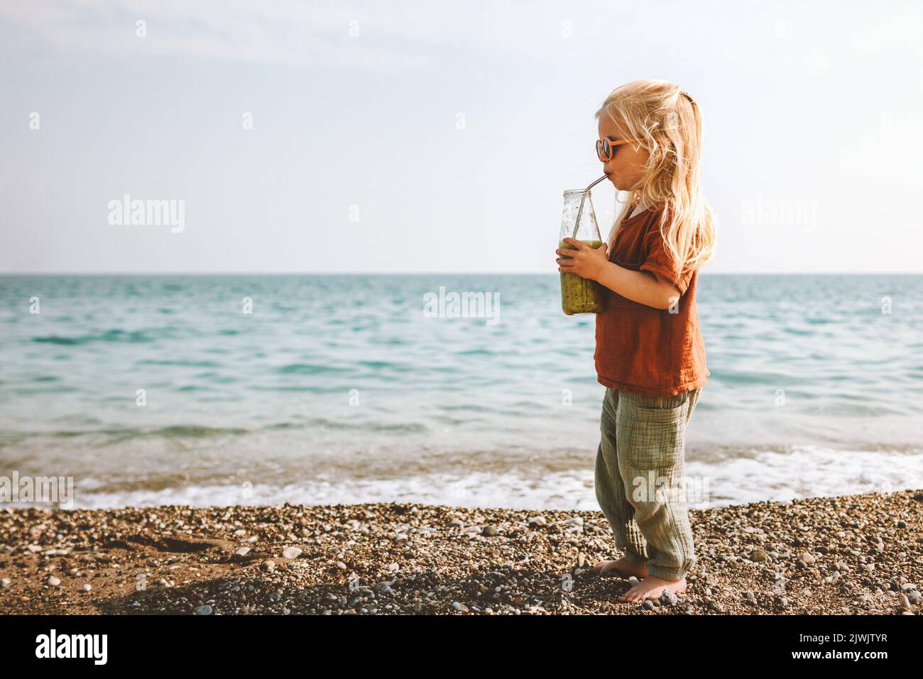 Kind trinkt Smoothie am Meeresstrand Kind mit Glasflasche gesunder Lebensstil veganes Essen Detox Getränk Sommer Familienurlaub Stockfoto