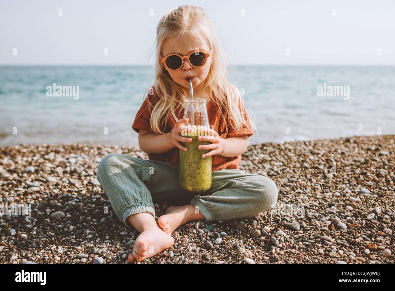 Kind trinkt frischen Smoothie im Freien am Strand gesunder Lebensstil Sommerferien Kindermädchen mit wiederverwendbarer Glasflasche veganes Bio-Essen Picknick Stockfoto