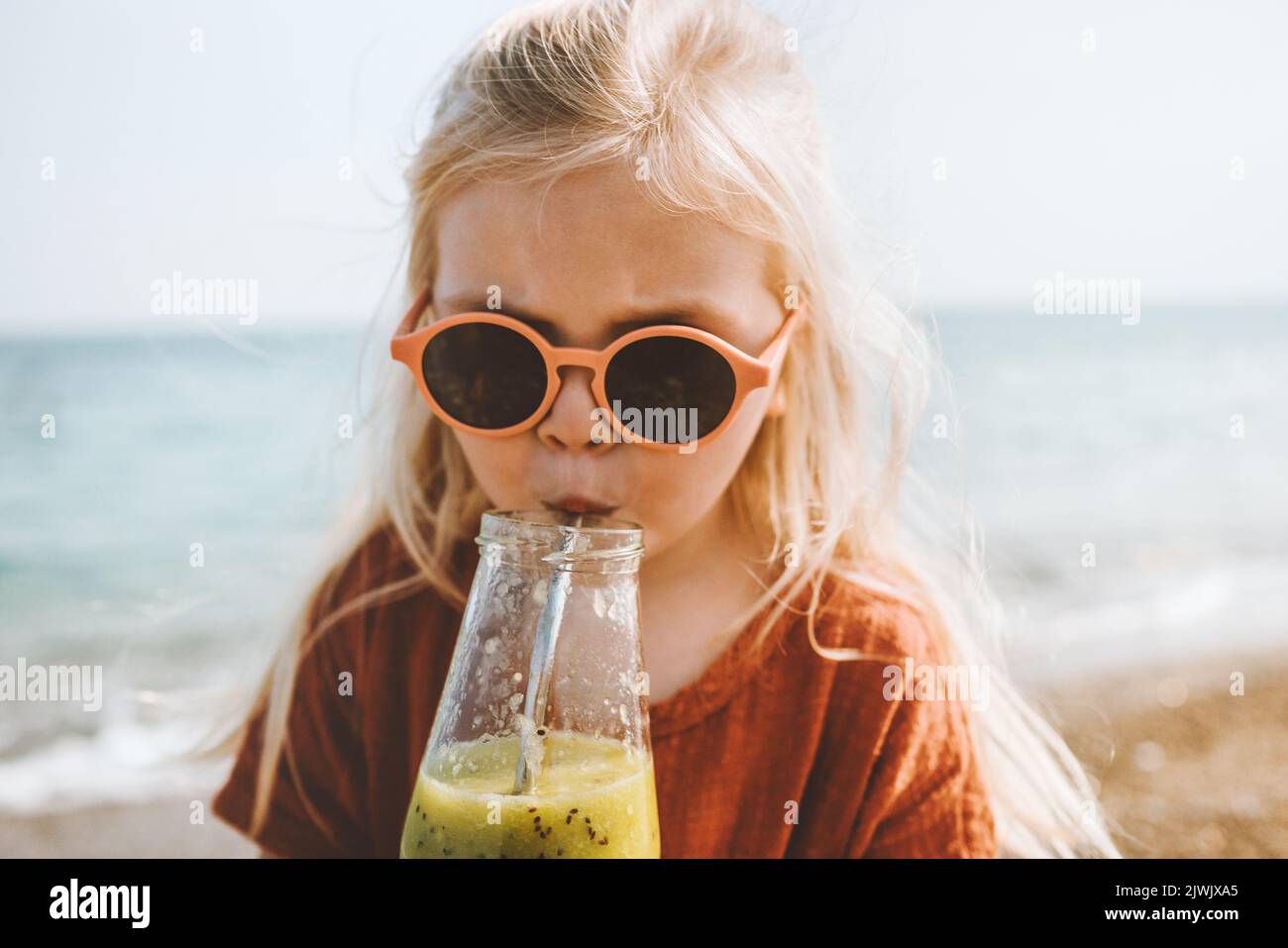 Kinder trinken Smoothie am Strand Sommerferien Frühstück gesund essen Lifestyle veganes Essen Mädchen mit Glasflasche und Sonnenbrille Stockfoto