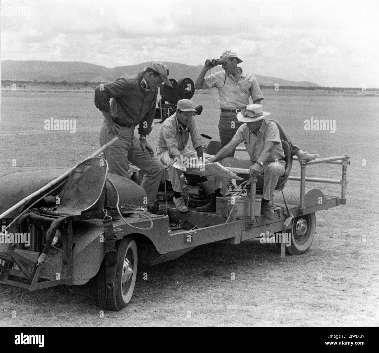 JOHN WAYNE Kameramann RUSSELL HARLAN (stehend) und Regisseur HOWARD HAWKS am Drehort Camera Car in Tansania, Afrika während der Dreharbeiten zu HATARI! 1962 Regisseur / Produzent HOWARD HAWKS Geschichte Harry Kurnitz Drehbuch Leigh Brackett Musik Henry Mancini Malabar / Paramount Picturs Stockfoto