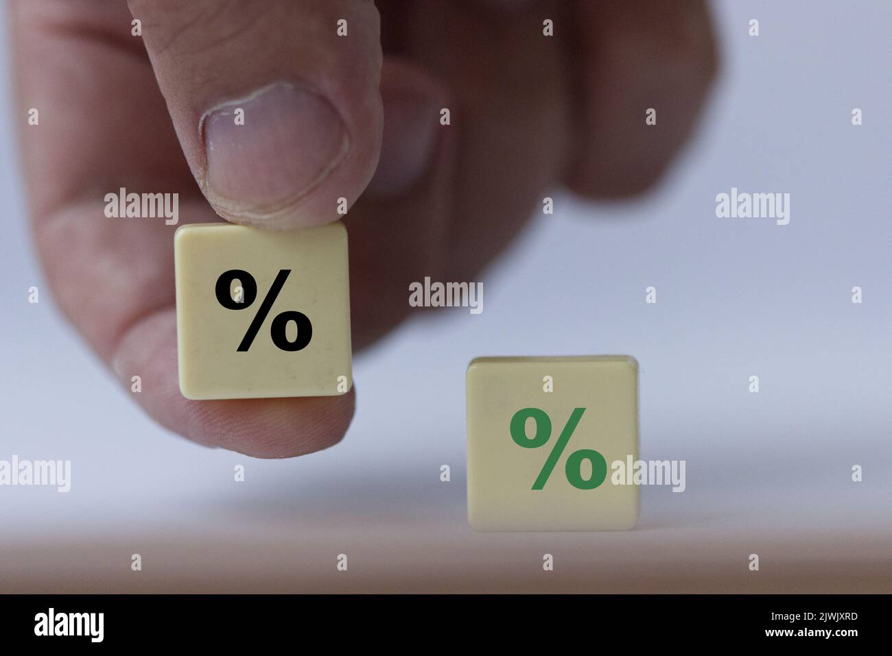 Hand hält ein Stück Scrabble mit schwarzem Prozentzeichen, das symbolisiert, dass die Zinssätze von positiv zu neutral werden. Stockfoto