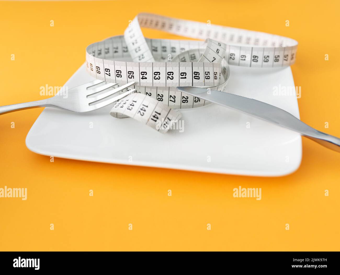 Maßband auf Platte mit Gabel und Messer auf orangenen Tischhintergrund mit Kopierraum, Diät und Gewichtsreduktion Konzept Stockfoto