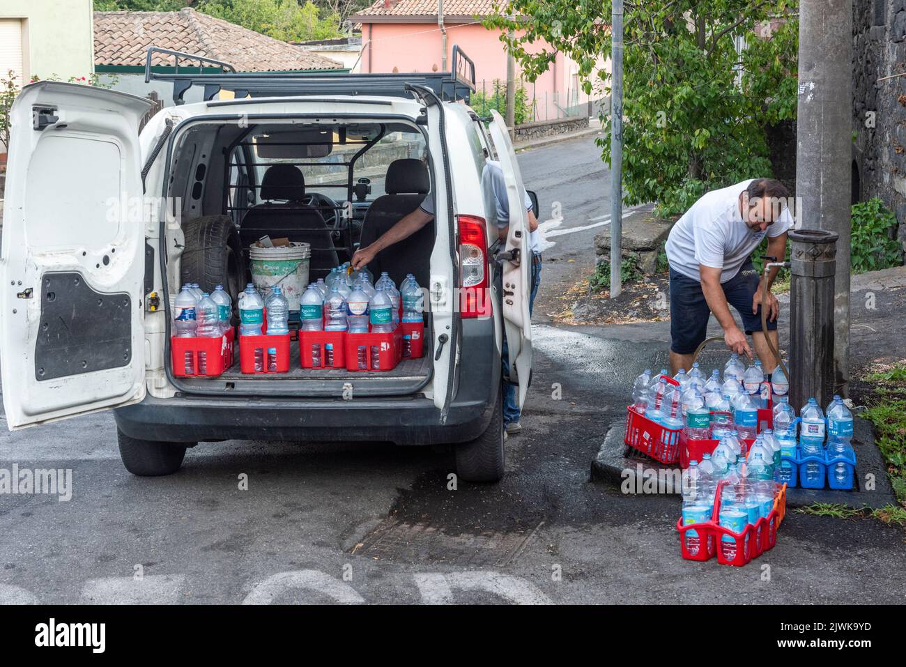 Füllen Sie Wasserflaschen mit frischem Trinkwasser aus einem öffentlichen Brunnen im sizilianischen Dorf Milo, hoch am Fuße des Ätna Stockfoto