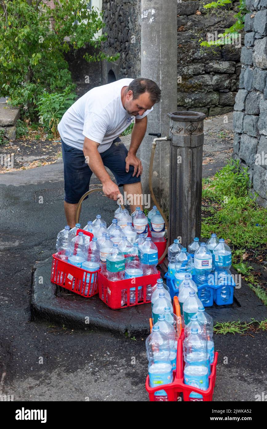 Füllen Sie Wasserflaschen mit frischem Trinkwasser aus einem öffentlichen Brunnen im sizilianischen Dorf Milo, hoch am Fuße des Ätna Stockfoto