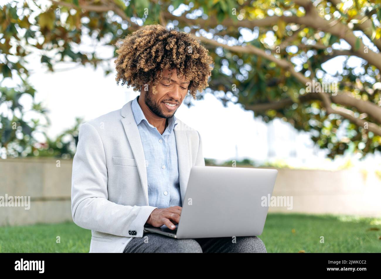 Positive smart erfolgreichen brasilianischen oder latino lockigen Mann, CEO, Programmierer, Content Manager, sitzen im Freien mit Laptop, arbeiten online an einem Projekt, Surfen im Internet, lächelnd glücklich Stockfoto