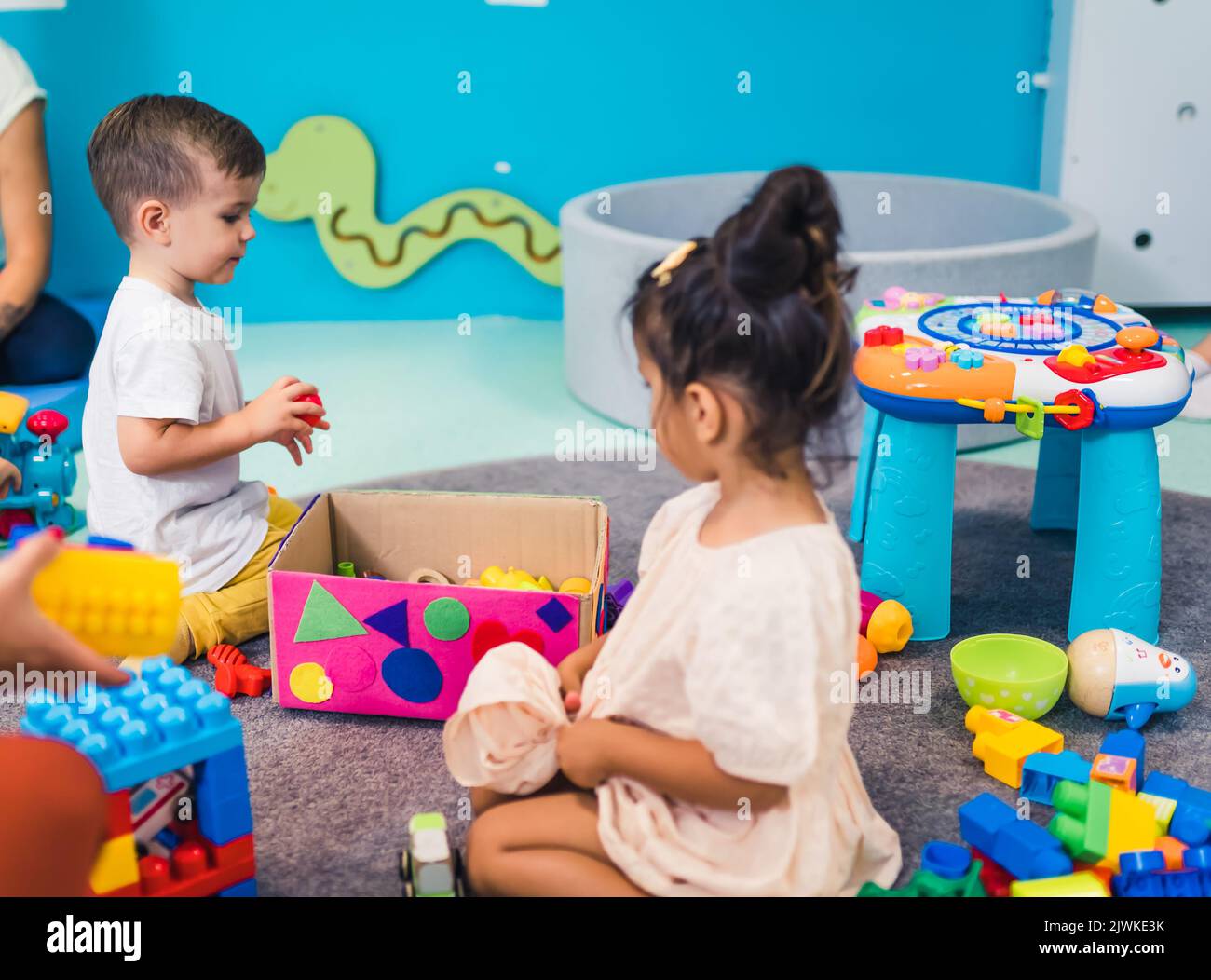 Vorstellungskraft und kreative Denkentwicklung. Kognitives Wachstum. Kleinkinder spielen mit bunten Plastikspielzeug und bunten Auto in einem Kindergarten Spielzimmer. Stockfoto