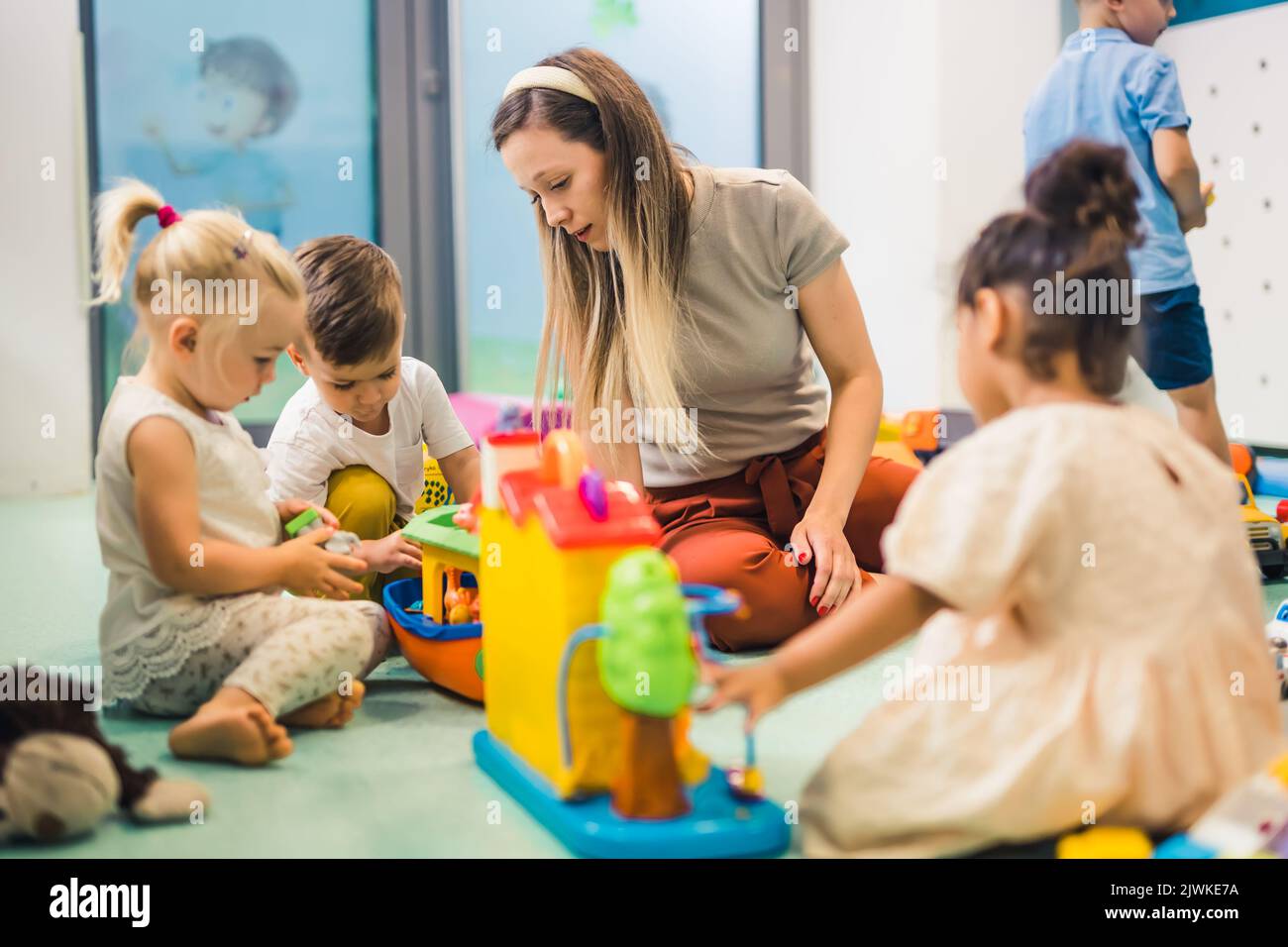 Kindergarten. Kleinkinder und ihre Lehrerin spielen mit bunten Plastikspielhäusern, Autos und Booten. Entwicklung von Phantasie, Kreativität, Feinmotorik und grobmotorischen Fähigkeiten. Hochwertige Fotos Stockfoto