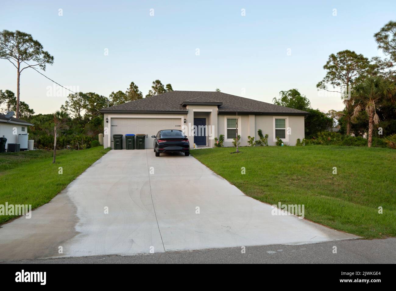 Das Auto parkte vor dem breiten Doppeltor der Garage auf der Betoneinfahrt des neuen modernen amerikanischen Hauses Stockfoto
