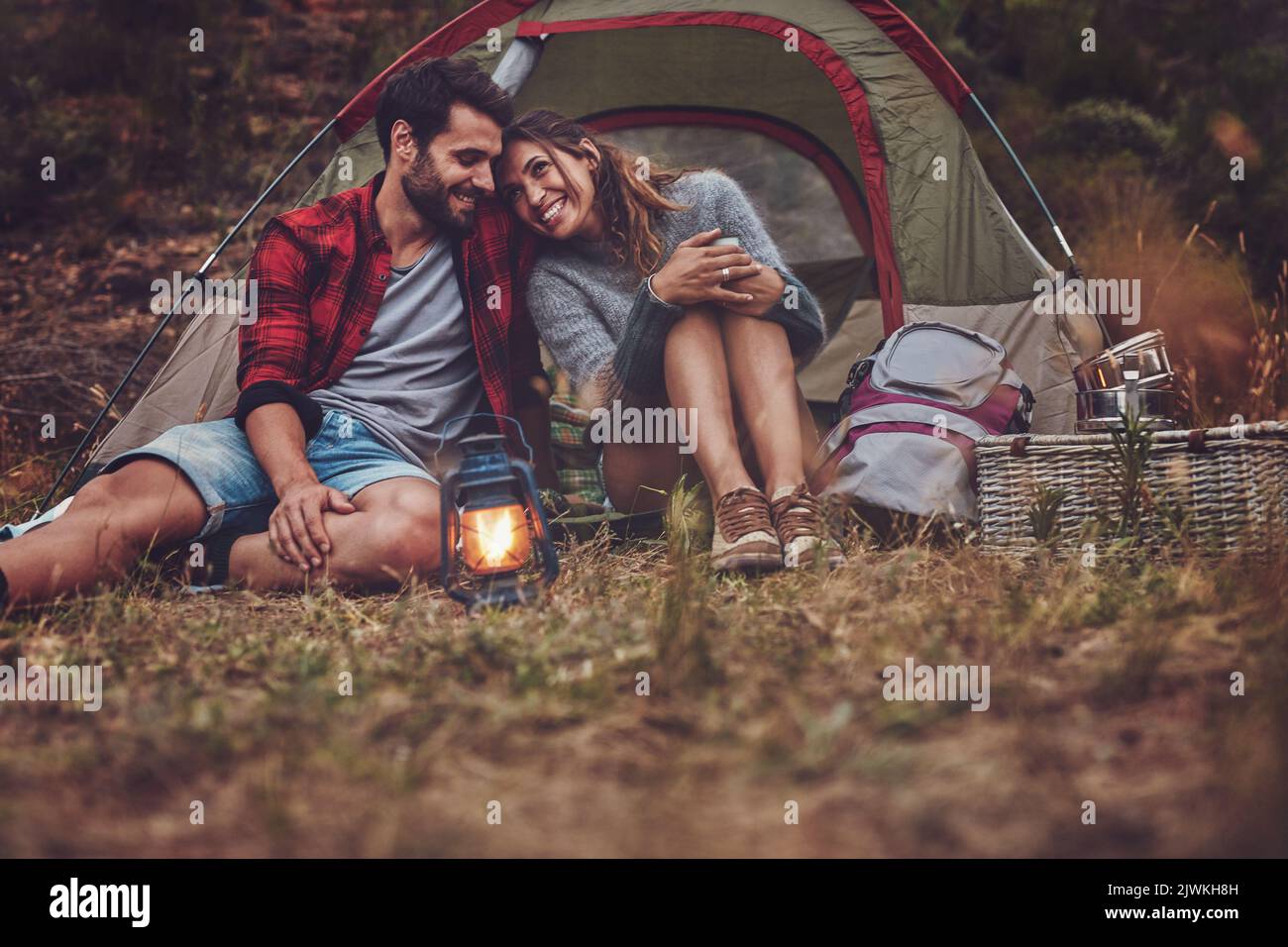 Romantisches Paar, das eine gute Zeit auf einem Campingurlaub verbringt. Liebevoller Mann und Frau, die abends mit einer Laterne vor ihrem Zelt sitzen. Stockfoto