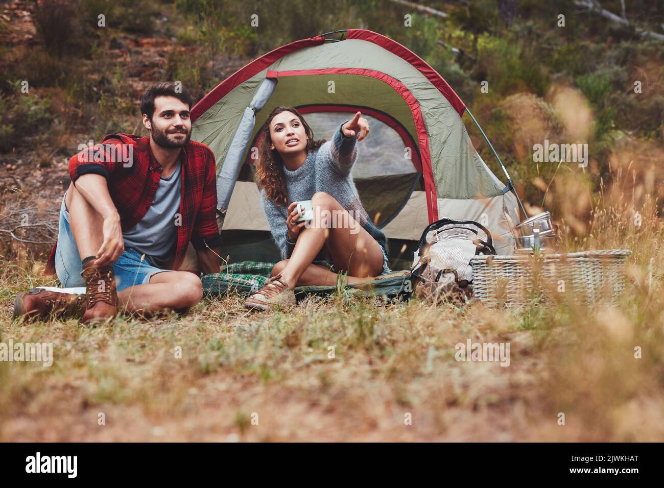 Junges Paar, das draußen vor einem Campingzelt sitzt. Junge Frau zeigt auf ihre Ansicht, während sie mit ihrem Freund kampt. Stockfoto