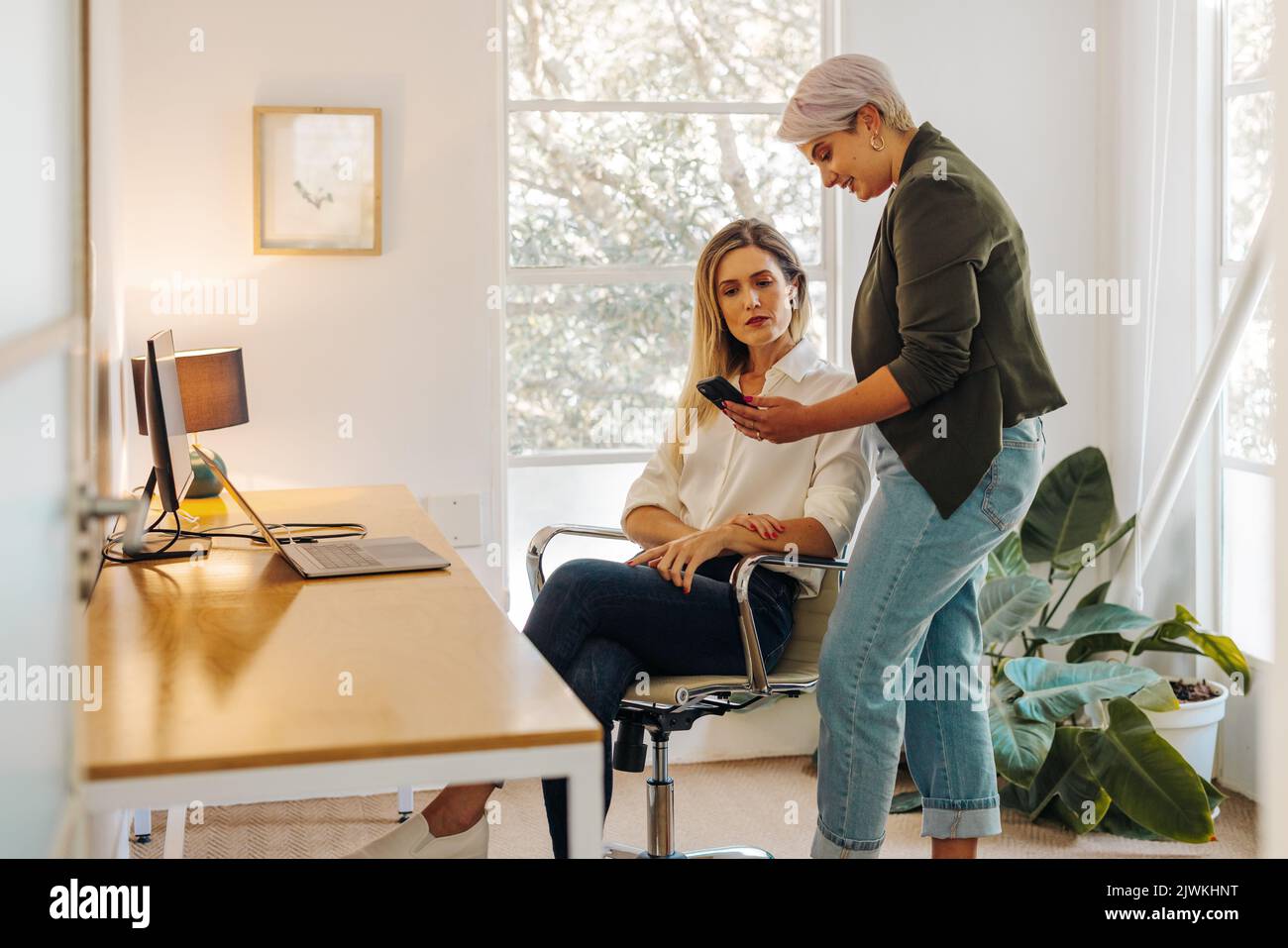 Junge Geschäftsfrau zeigt ihrem Kollegen in einem modernen Büro ihren Smartphone-Bildschirm. Zwei junge Geschäftsfrauen arbeiten in einer eigenen Frau an einer neuen Aufgabe zusammen Stockfoto
