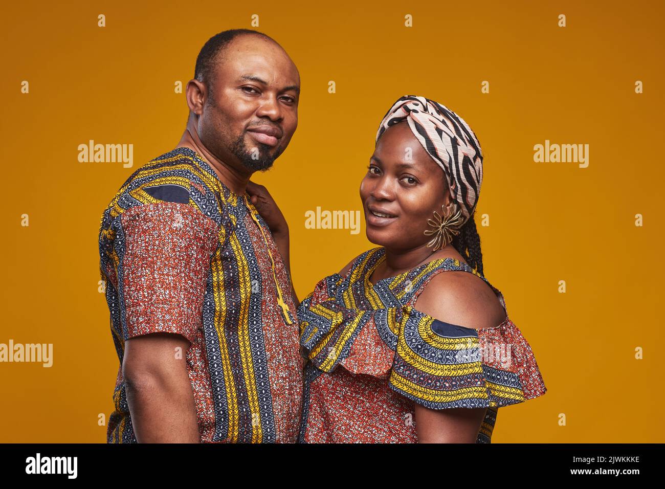 Porträt eines afrikanischen Paares in Nationalkostümen, das vor der Kamera vor gelbem Hintergrund lächelt Stockfoto